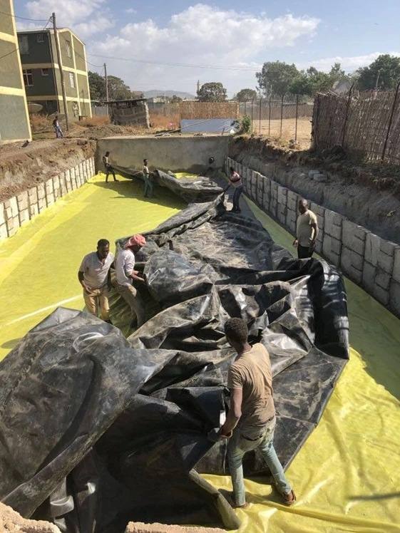 Workers unrolling the black PE liner over the yellow protection cloth in the walled wetland basin