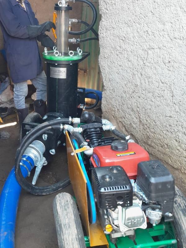 A trained operator running a portable PuPu pit-emptying pump in a narrow passage between houses