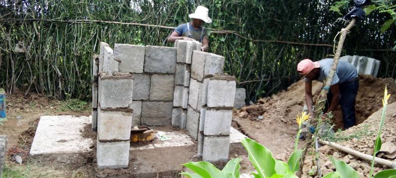 Two artisans building a household toilet from interlocking panels while digging the pit